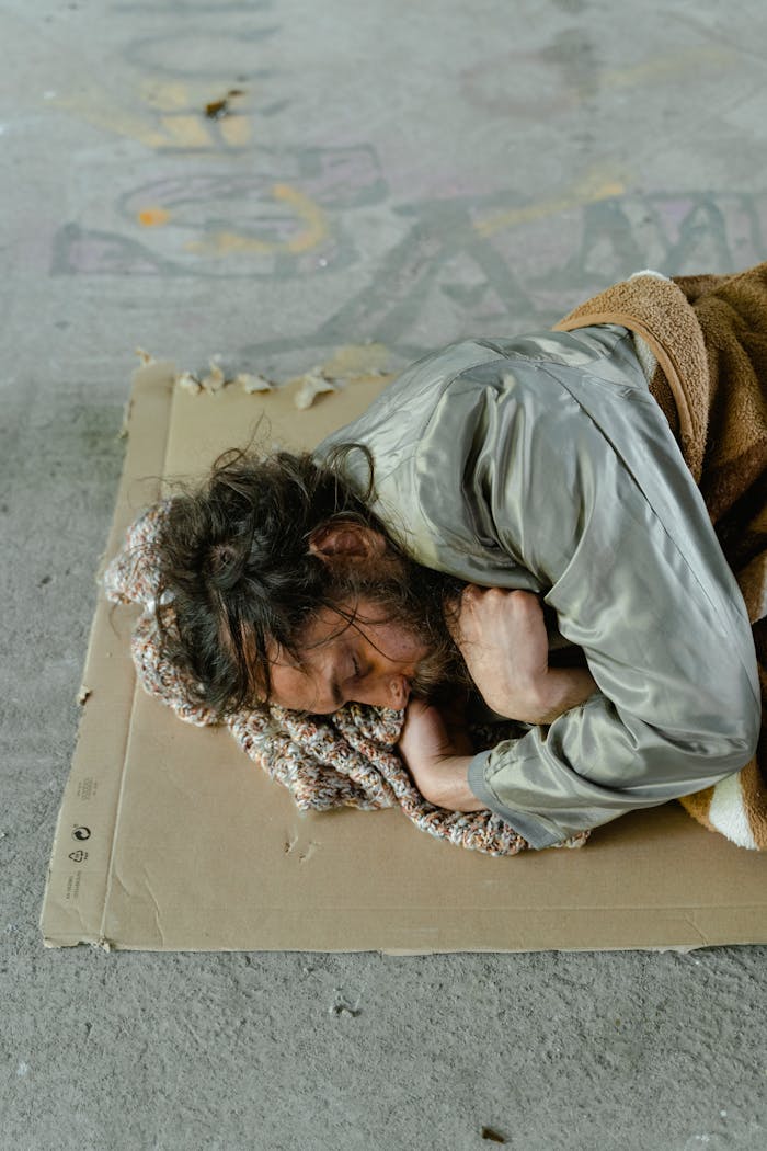 Homeless man sleeping on a cardboard in an urban setting.