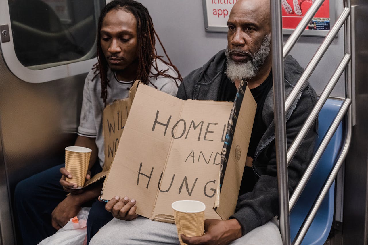 Two men holding signs about homelessness in a subway train emphasize urban hardship.